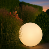 Glowing spherical light fixture in a garden setting with evening sky.